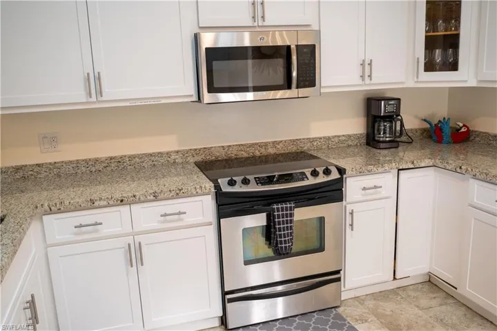 Kitchen featuring stainless steel appliances, white cabinets, glass insert cabinets, and light stone counters