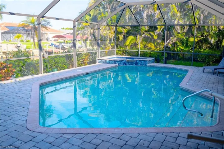 Outdoor pool featuring pool enclosure, a patio, and an in ground hot tub