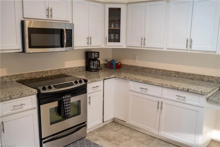 Kitchen with appliances with stainless steel finishes, white cabinetry, glass insert cabinets, and light stone counters