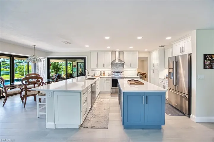 Kitchen with stainless steel appliances, white cabinets, recessed lighting, wall chimney exhaust hood, and blue cabinets