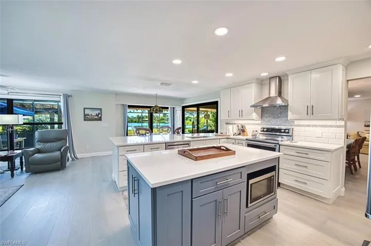 Kitchen with white cabinets, wall chimney range hood, stainless steel appliances, tasteful backsplash, and light stone countertops