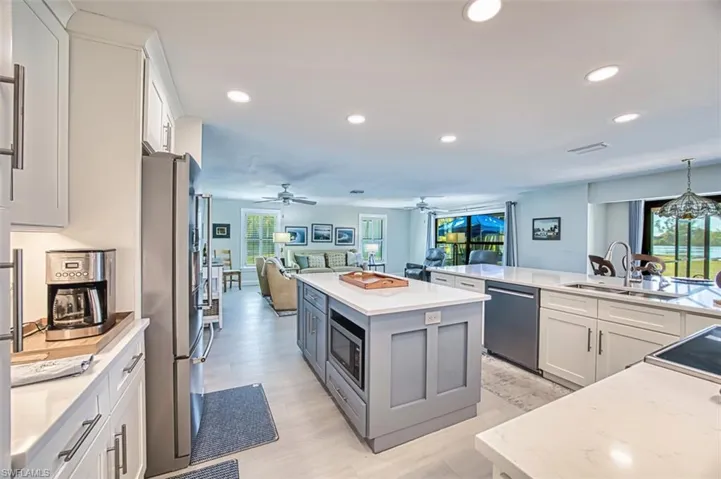 Kitchen with white cabinetry, open floor plan, light stone countertops, stainless steel appliances, and gray cabinets