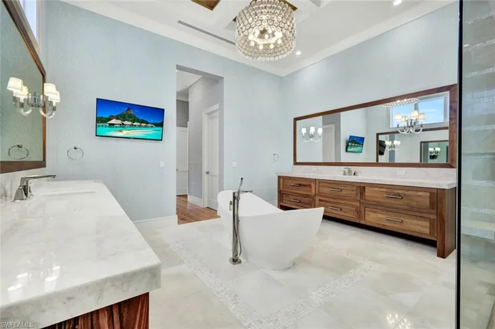 Bathroom with suspended lighting, two vanities, coffered ceiling, a soaking tub, and inlaid floor details