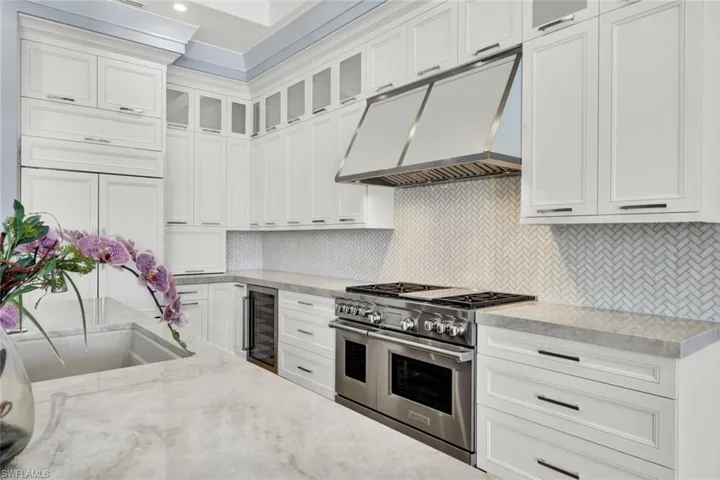 Kitchen with glass fronted cabinets, double oven range, light stone counters, wine cooler, and white cabinets