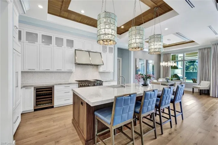 Two tone kitchen with a tray ceiling, a kitchen bar, dual tone cabinets, glass insert cabinets, and light stone countertops
