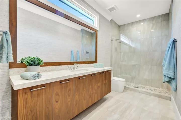 Full bath with vanity, a tile shower, and light tile patterned flooring