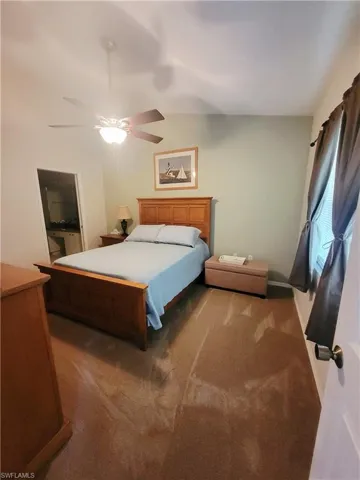 Carpeted bedroom with ceiling fan, vaulted ceiling, and ensuite bath
