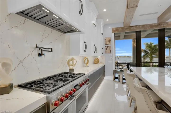 Kitchen with premium range hood, range with two ovens, decorative backsplash, white cabinetry, and beamed ceiling - Virtually Edited Image