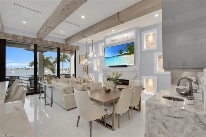 Dining area featuring a glass covered fireplace, beamed ceiling, recessed lighting, a water view, and light tile patterned floors - Virtually Edited Image