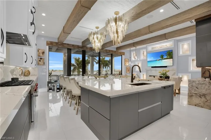 Kitchen with modern cabinets, a large island with sink, light stone countertops, beam ceiling, and recessed lighting - Virtually Edited Image