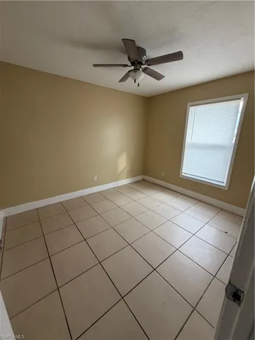 Empty room with light tile patterned floors, a ceiling fan, and a textured ceiling