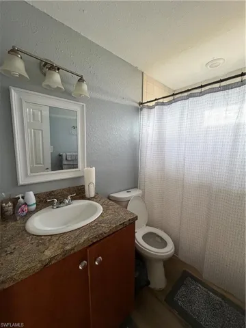 Bathroom featuring a textured wall, a textured ceiling, a shower with shower curtain, vanity, and dark wood-style floors