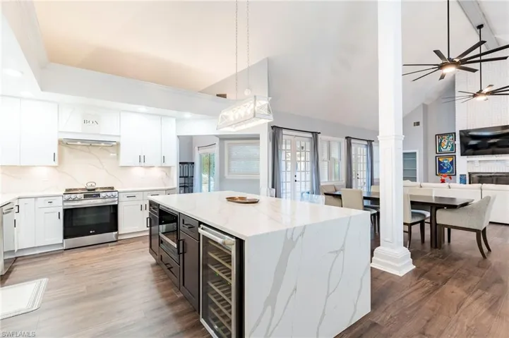 Kitchen featuring two tone cabinets, light stone countertops, vaulted ceiling, open floor plan, and tasteful backsplash