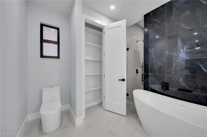 Full bathroom featuring toilet, baseboards, a spacious closet, a soaking tub, and a stall shower