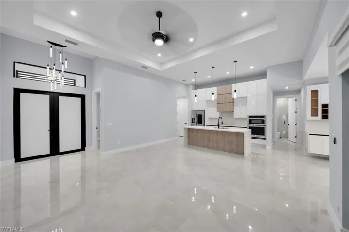Unfurnished living room featuring baseboards, a raised ceiling, ceiling fan with notable chandelier, french doors, and recessed lighting