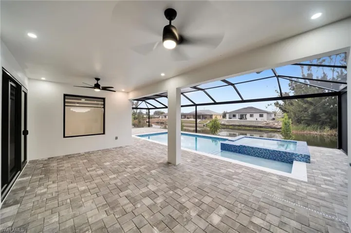 View of pool featuring a pool with connected hot tub, a patio area, ceiling fan, and glass enclosure