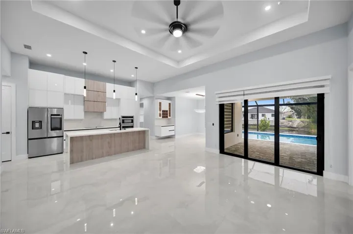 Kitchen with a kitchen island with sink, light countertops, stainless steel fridge with ice dispenser, a tray ceiling, and modern cabinets
