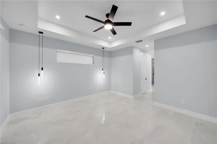 Empty room with a tray ceiling, recessed lighting, visible vents, and baseboards