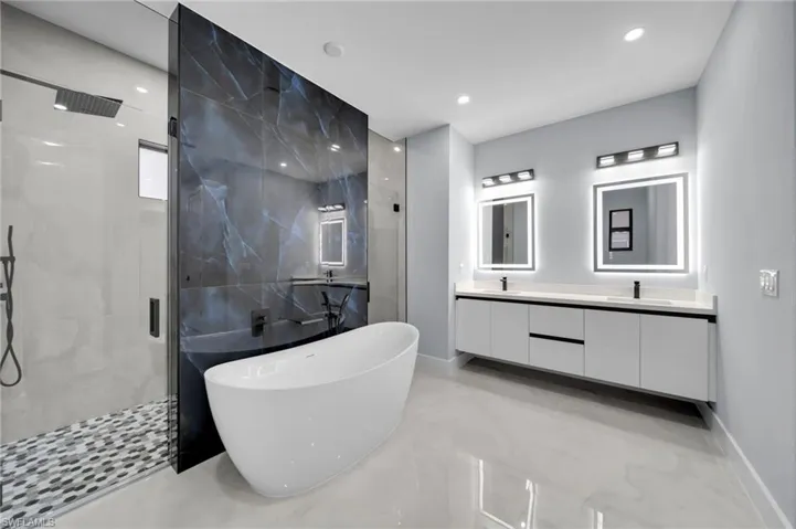 Bathroom with double vanity, a stall shower, a soaking tub, a sink, and recessed lighting