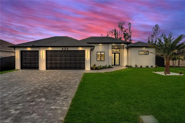 Prairie-style home featuring a garage, fence, decorative driveway, a yard, and stucco siding