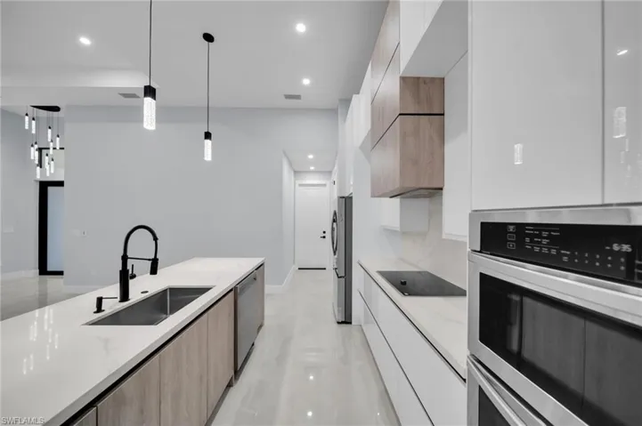Kitchen with modern cabinets, light stone counters, decorative light fixtures, stainless steel appliances, and a sink