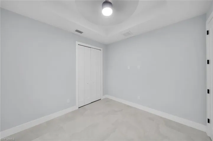 Unfurnished bedroom featuring a tray ceiling, a closet, visible vents, and baseboards
