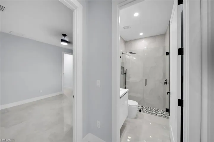 Bathroom with a marble finish shower, visible vents, toilet, vanity, and baseboards