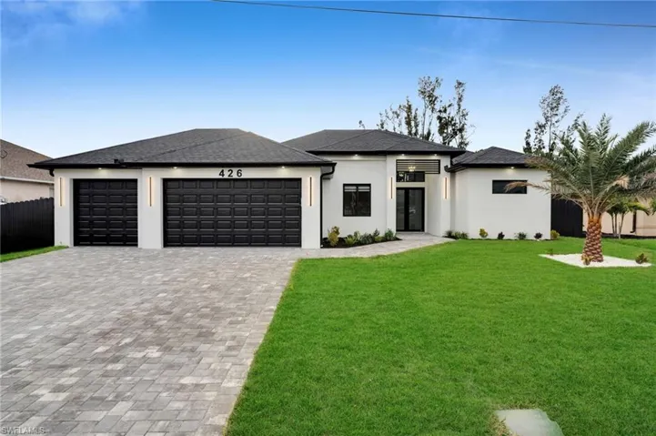 Prairie-style home featuring decorative driveway, stucco siding, a front yard, fence, and a garage