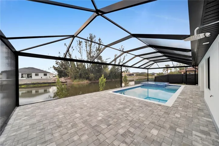 View of pool with glass enclosure, a pool with connected hot tub, a water view, and a patio