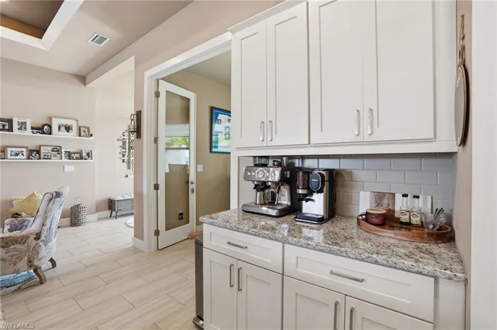 Kitchen with light stone counters, white cabinetry, decorative backsplash, and wood ceramic tiled floors