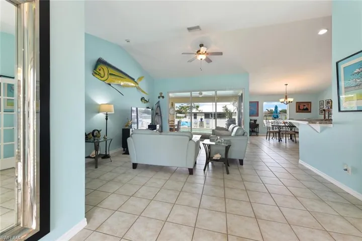 Living room with light tile patterned flooring, a ceiling fan, a chandelier, and vaulted ceiling