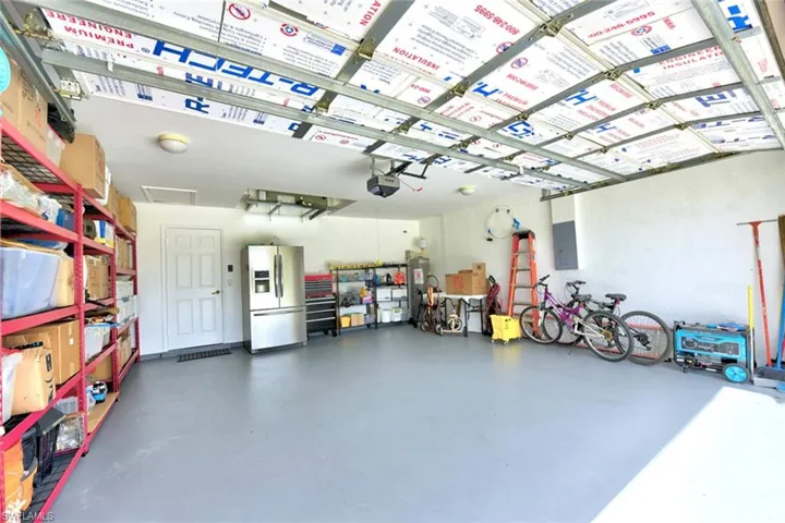 Garage featuring stainless steel refrigerator with ice dispenser, electric panel, and water heater