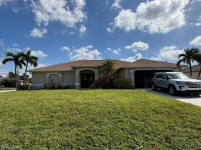 View of front of house with a front yard, stucco siding, driveway, and an attached garage