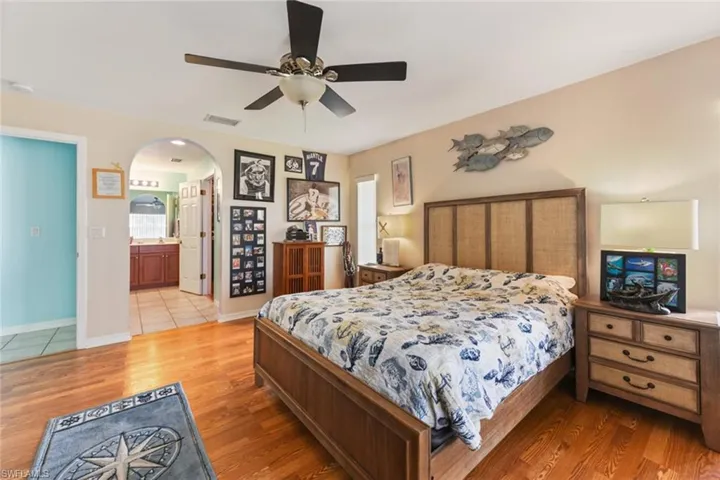 Bedroom with light wood-type flooring, ceiling fan, arched walkways, and ensuite bathroom