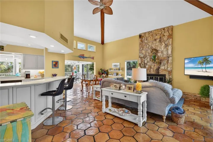 Living room featuring high vaulted ceiling, a ceiling fan, a stone fireplace, and beam ceiling