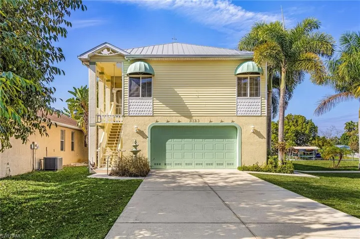 View of front of home with stairway, a front yard, concrete driveway, and a balcony