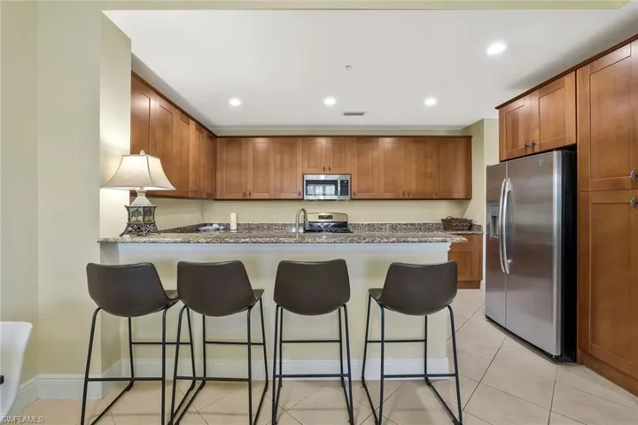 Kitchen with appliances with stainless steel finishes, recessed lighting, a peninsula, light tile patterned floors, and a kitchen bar
