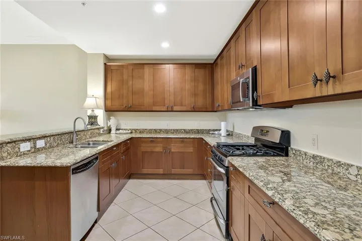 Kitchen featuring stainless steel appliances, brown cabinets, a peninsula, light tile patterned flooring, and recessed lighting