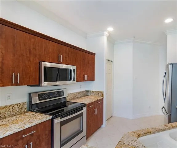 Kitchen featuring crown molding, stainless steel appliances, light stone counters, and light tile flooring.
