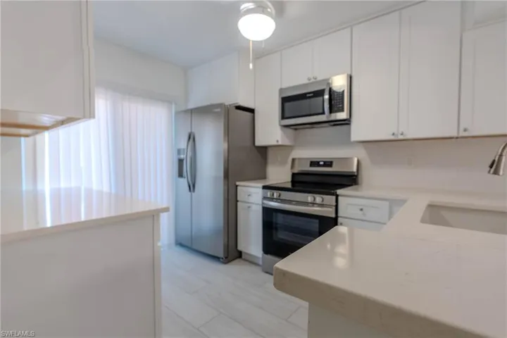 Kitchen featuring stainless steel appliances, white cabinetry, and light stone countertops