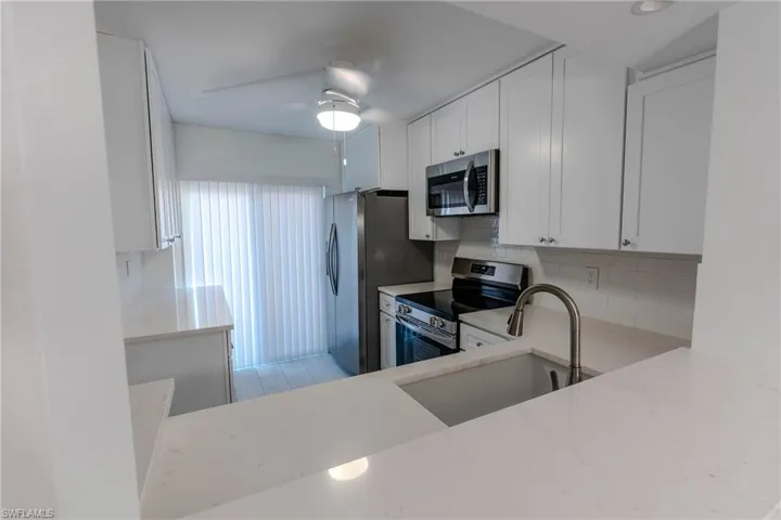 Kitchen featuring white cabinetry, stainless steel appliances, light stone countertops, backsplash, and ceiling fan