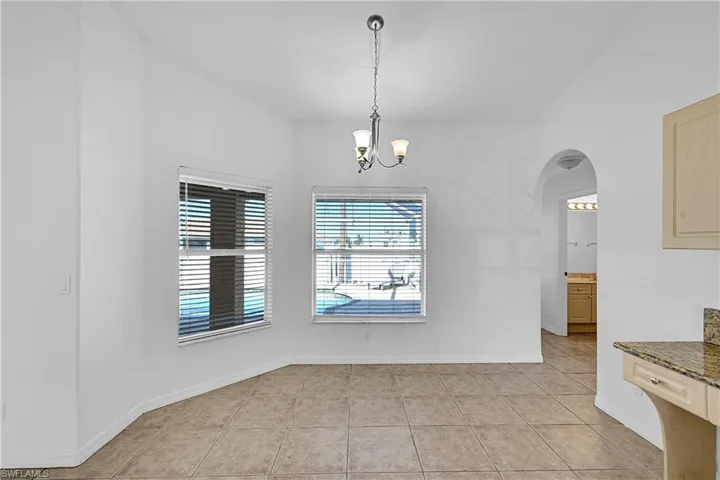 Unfurnished dining area with arched walkways, light tile patterned floors, and a chandelier