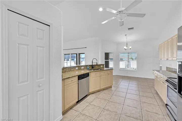 Kitchen with light tile patterned floors, appliances with stainless steel finishes, light stone counters, light brown cabinets, and a chandelier