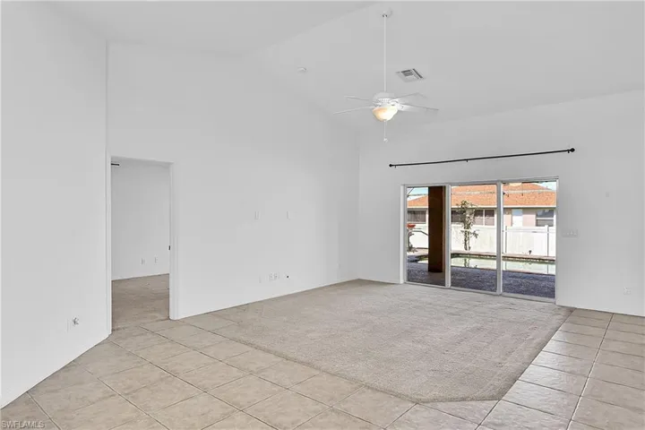 Spare room featuring high vaulted ceiling, light tile patterned flooring, ceiling fan, and light colored carpet