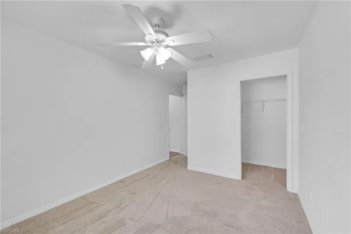 Unfurnished bedroom with light carpet, a ceiling fan, and a walk in closet