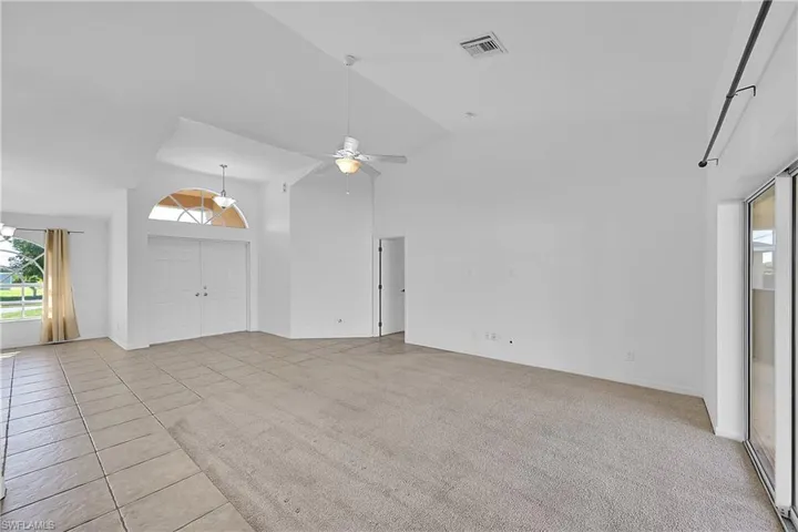 Unfurnished living room with healthy amount of natural light, high vaulted ceiling, light carpet, light tile patterned floors, and ceiling fan