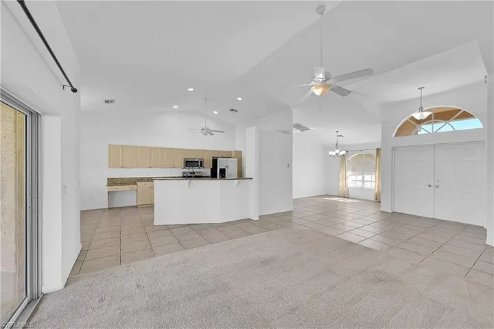 Unfurnished living room with a ceiling fan, light tile patterned floors, high vaulted ceiling, a chandelier, and recessed lighting