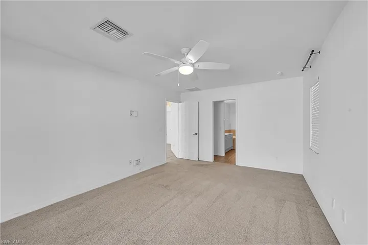 Unfurnished bedroom with light carpet, ensuite bath, and a ceiling fan