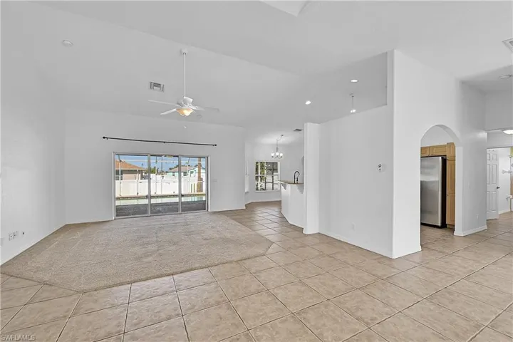 Spare room with light tile patterned flooring, ceiling fan, light carpet, lofted ceiling, and a chandelier
