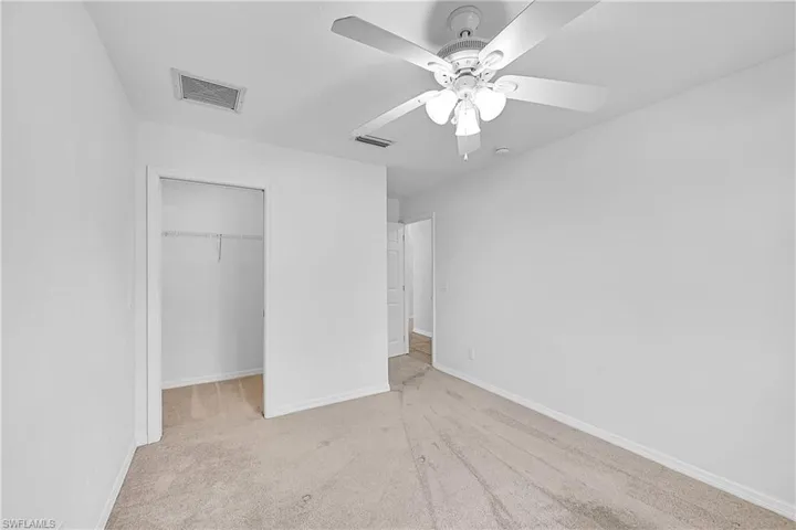Unfurnished bedroom featuring light carpet, a spacious closet, and a ceiling fan